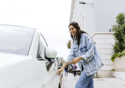 Happy young woman opening the door of a hired car