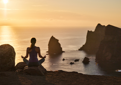 Mulher a meditar no topo de uma falésia