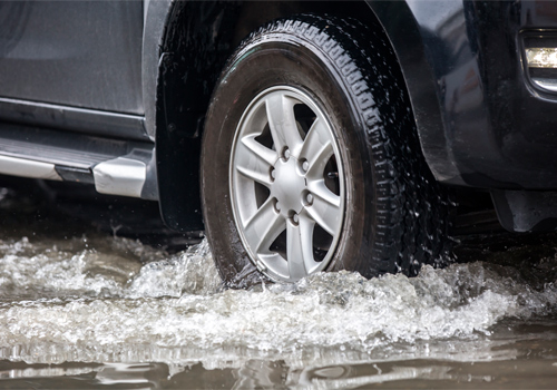 Close-up of a car wheel driving through a flooded street.