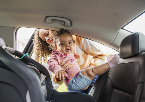 Mother placing her baby in a car seat facing the rear