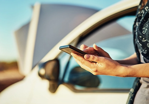 Pessoa junto a um carro com capot aberto a utilizar o telemóvel para fazer uma reserva de uma outra viatura.