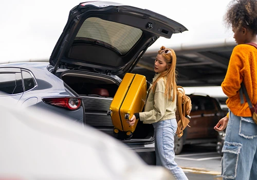 Two travellers placing luggage in the trunk of a rental car at the airport before starting their trip.