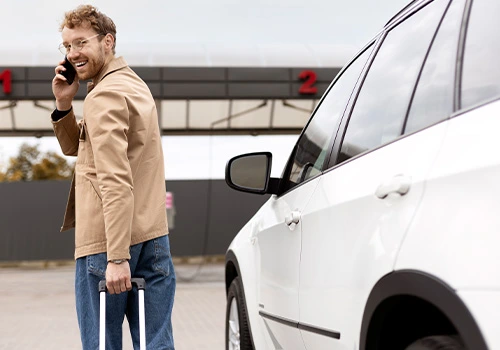 Traveller with a suitcase next to a rental car at airport after picking up the vehicle to explore the city.