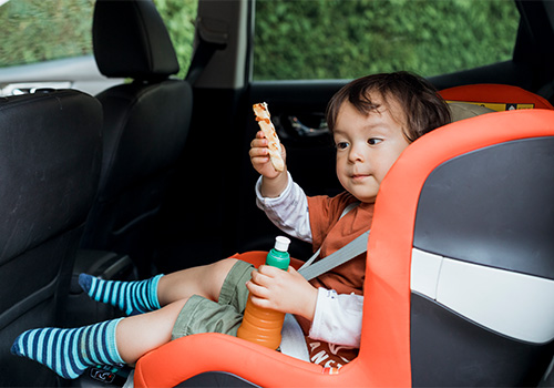 young boy in a carseat with a snack