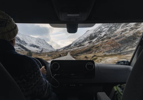 Homem a conduzir um carro numa estrada de montanha coberta de neve. 