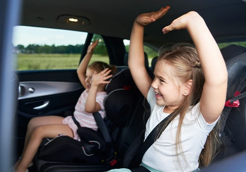 Two children sitting in the back seat of the car with their arms up in the air.