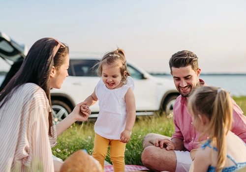 Family having a picnic outdoors, with a car in the background