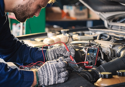 Mechanic testing car battery voltage with a multimeter to check performance and car battery life.