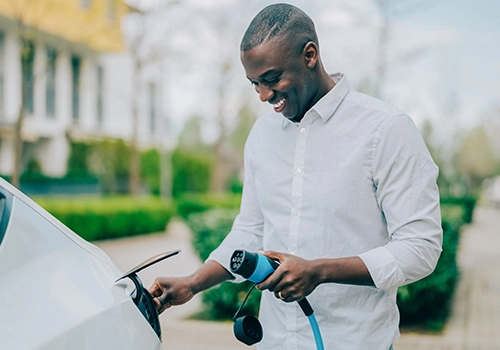 Man smiling while charging an electric car on the street, with the cable connected to the side port.