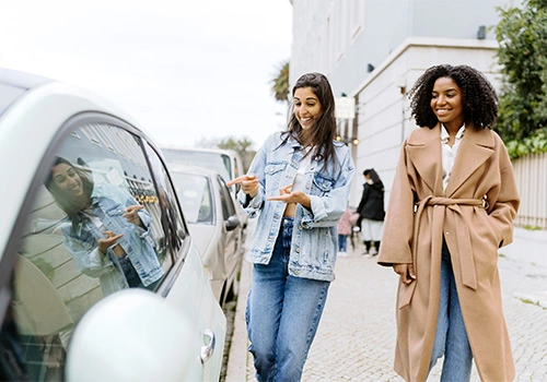 Duas mulheres junto a um carro na cidade, a planear deslocações urbanas durante a Lisboa Fashion Week.
