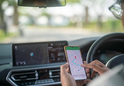 Driver behind the wheel of a fleet vehicle consulting a GPS navigation system on a smartphone, integrated with route management technology.