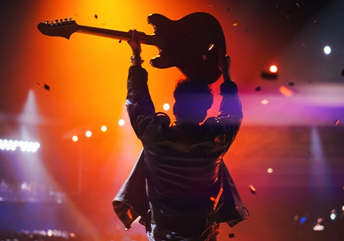Artist on stage raising a guitar under intense lights during a live music festival concert.