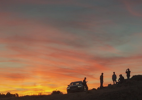 Group of friends with a car at sunset, enjoying a scenic stop during a road trip