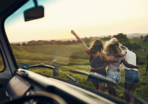 Friends enjoying countryside views during a road trip, standing beside a parked car