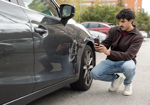 Man photographing damage to a rental car to activate insurance