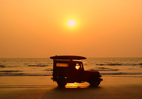 car on the beach with a surfboard and the sunset in background.