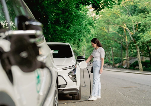Employee charging an electric car on a tree-lined street, linking electric mobility to corporate sustainability.