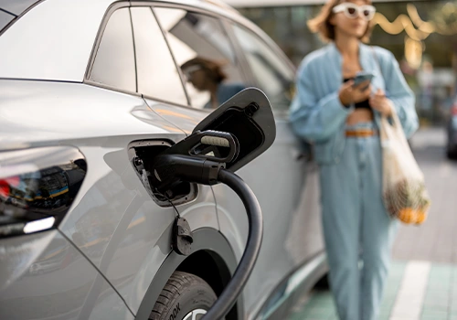 Electric car charging on a public street, with charging cable connected and user in the background, in an urban setting.