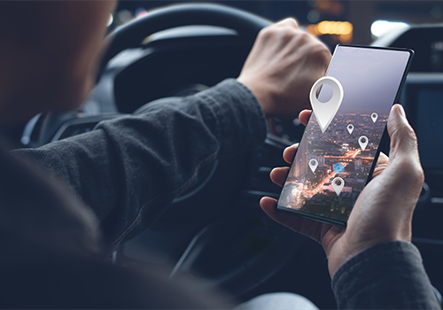 Condutor com telemóvel na mão com ícones de localização a saírem do ecrã.