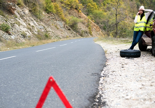 Warning triangle on the road and driver wearing a reflective vest next to a stopped car.