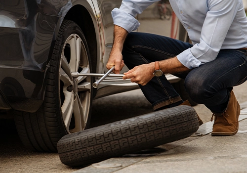 Driver loosening wheel nuts while changing a tire using a wrench.