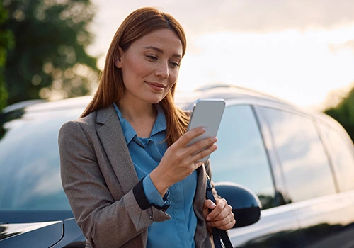 Profissional junto a um carro ao ar livre, a usar o telemóvel para gerir opções de viaturas para PME.