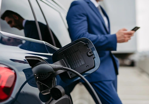 Carro elétrico a carregar, com um empresário em segundo plano.