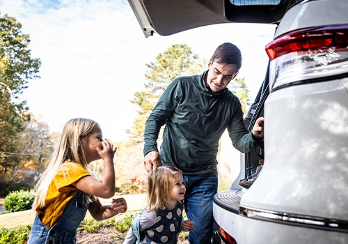 Pai e filhas a colocar malas no carro antes de uma viagem de fim de semana