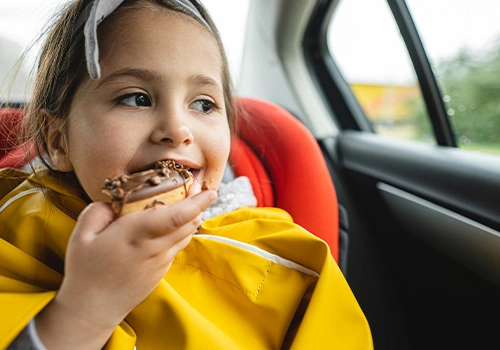 Criança a comer chocolates no banco de trás do carro. 