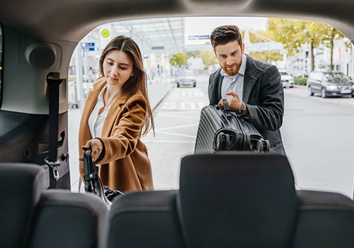 Executive couple on a business travel trip placing luggage in the rental vehicle before a meeting.