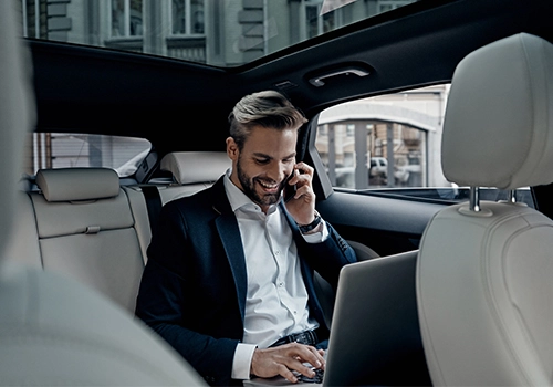 Executive on a business travel trip working on a laptop and mobile phone inside the vehicle, in the back seat.