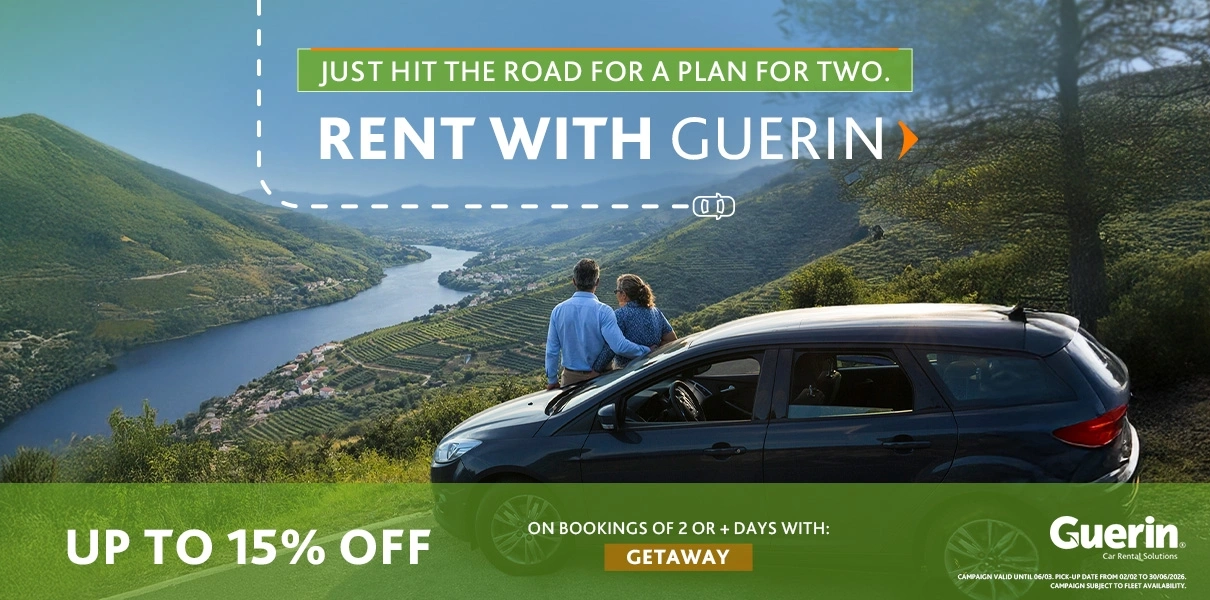 Couple sitting next to a car at a viewpoint overlooking a valley and river, with Guerin promotional text: &lsquo;Rent with Guerin,&rsquo; up to 15% discount on bookings of 2+ days with the code GETAWAY.